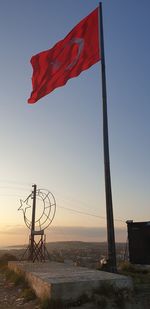 Red flag on pole against sky during sunset