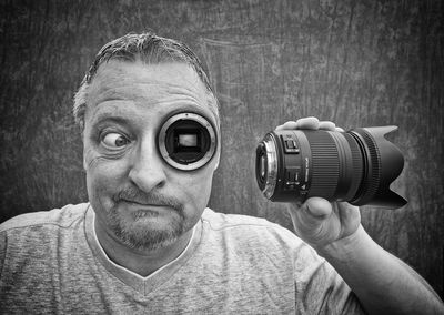 Digital composite image of mature man with photographic eye holding camera lens