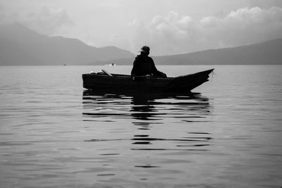 Silhouette man sitting on boat in sea against sky