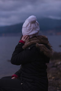 Woman looking away while sitting by lake against sky