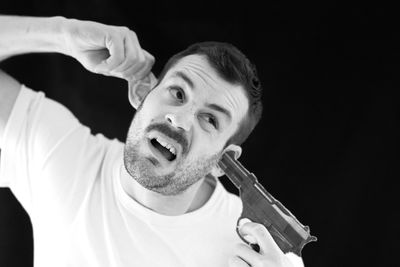 Man pointing gun in ear against black background