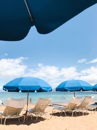Empty lounge chairs by blue parasols at sandy beach