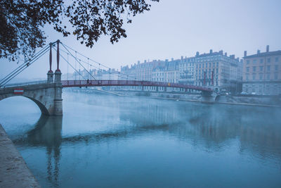 Bridge over misty river with city in background