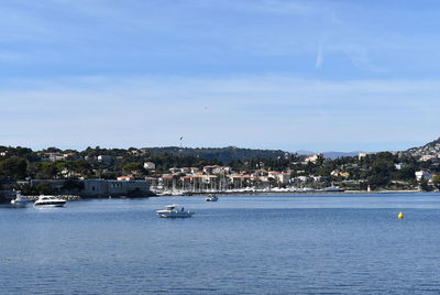 Sailboats in sea by townscape against sky