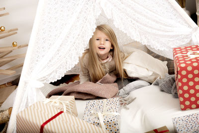 Happy girl child between pillows and christmas gift boxes