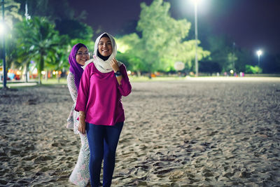 Portrait of smiling sisters standing on beach at night