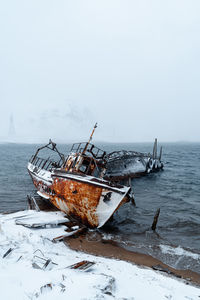 Damaged ship in sea against sky during winter