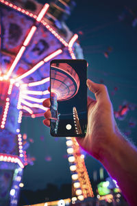 Midsection of person holding illuminated carousel at amusement park