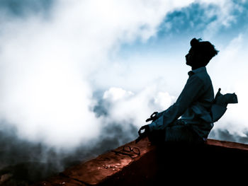 Low angle view of man sitting on mountain against sky