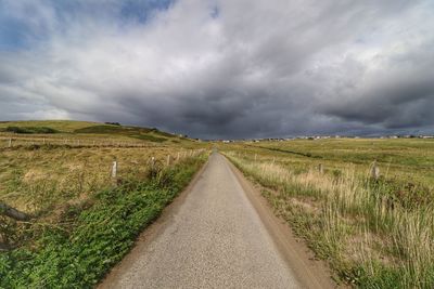 Empty road amidst field against sky