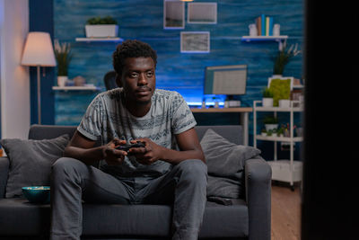 Young man playing video game sitting on sofa at home