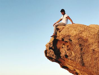 Low angle view of man sitting on rock formation against clear sky