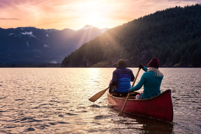 Rear view of men on lake against sky during sunset