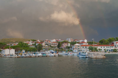 Scenic view of rainbow over river by buildings in city against sky