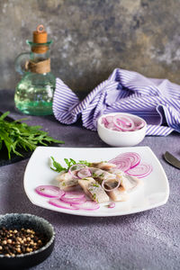 Sliced salted herring with onions and arugula on a plate on the table. simple snack. vertical view