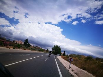 Rear view of person riding motor scooter on road