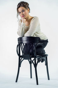 Portrait of woman sitting on chair against white background