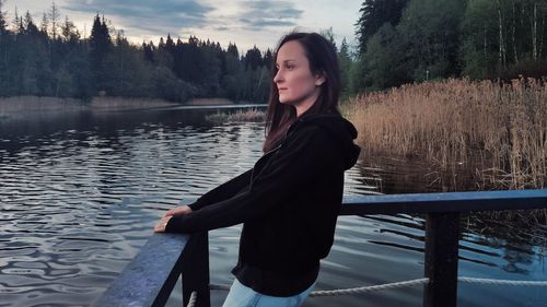 Young woman looking at lake against trees