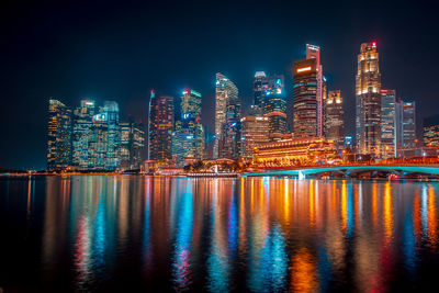 Illuminated buildings by river against sky at night