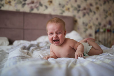 Charming baby, 6 months old, lies crying on his stomach on a bed in a bright,