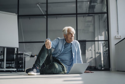 Thoughtful businessman looking away while sitting by laptop in office