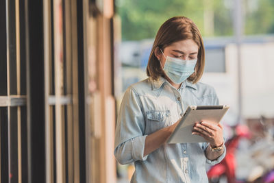 Woman wearing mask using digital tablet outdoors