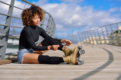 Young woman sitting on railing against sky