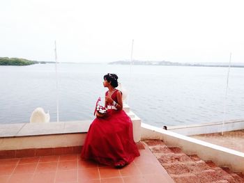 Rear view of woman sitting by sea against sky