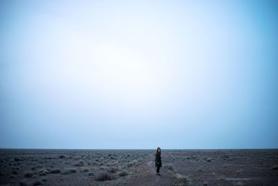 Rear view of man standing on field against clear sky