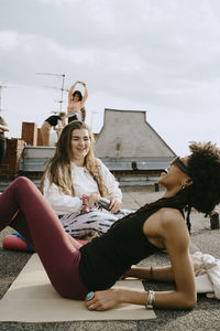 Smiling young woman talking with cheerful female friend reclining on exercise mat