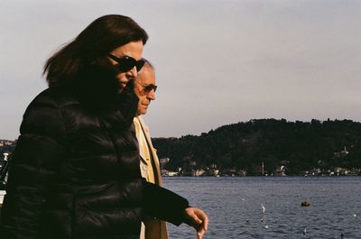 Side view of young man wearing sunglasses standing against sky