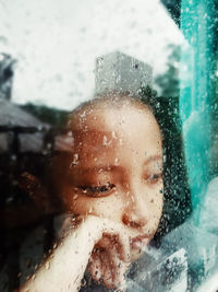 Thoughtful girl seen through wet glass window