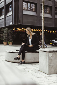 Businesswoman with in-ear headphones looking away while sitting outdoors