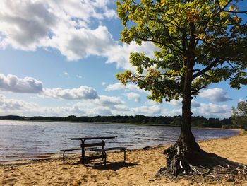 Empty bench by lake against sky