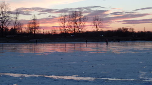 Silhouette bare trees by lake against sky during sunset