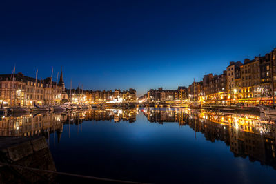 Illuminated buildings by river against sky at night