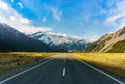Road by mountains against sky during winter