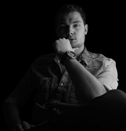 Portrait of confident young man sitting against black background