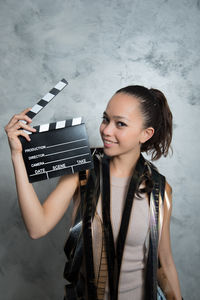 Portrait of woman holding clapperboard while standing against wall