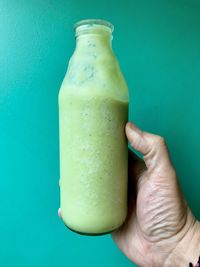 Close-up of hand holding drink against blue background