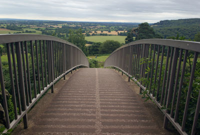 Footbridge amidst trees against sky