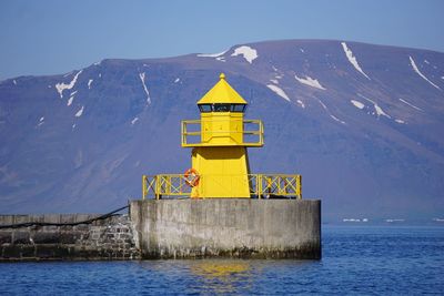 Yellow lighthouse by river against mountains on sunny day