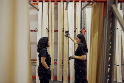 Multiracial female colleagues discussing over planks at rack in lumber industry