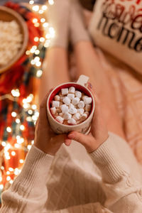 Cup of cocoa or coffee drink with marshmallows in female holding hands over the legs of woman