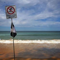 Information sign on beach against sky