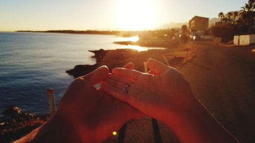 Cropped hands of couple by sea during sunset