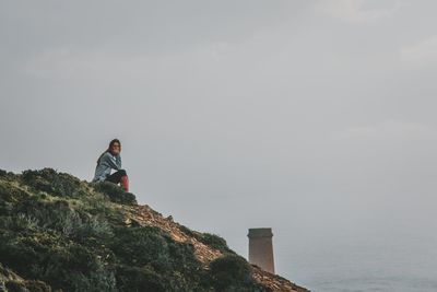 Man sitting on rock looking at sea against sky