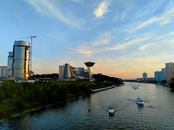 Boats in river by buildings in city against sky