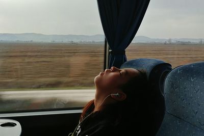 Side view of boy sleeping while sitting by window in train