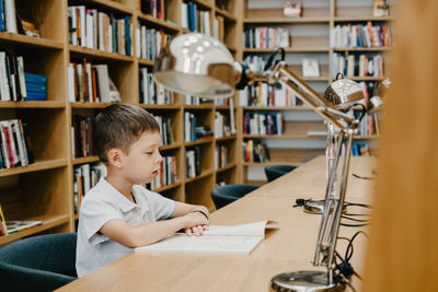 Schoolboy sitting on table and reading book in library at school. preparing for homework. 